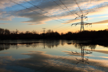 Electricity pylon with reflection in water at sunset