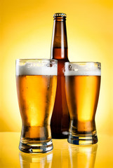 Two glasses and Bottle of fresh light beer on yellow background