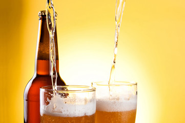 Beer Being Poured in Two glasses and Bottle on yellow background
