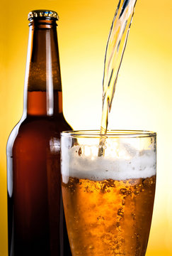 Beer Being Poured in Glass and Bottle on yellow background