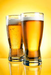 Two glasses of beer close-up with froth over yellow background