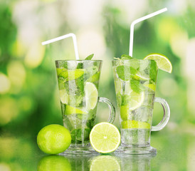 Glasses of cocktail with lime and mint on green background