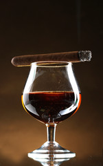 glass of brandy and cigar on brown background