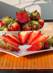 Ganze und halbe Erdbeeren in einer Schale und auf einem Teller