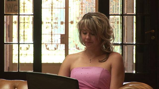 Junge Frau im Abendkleid arbeitet am Computer auf der Sofa