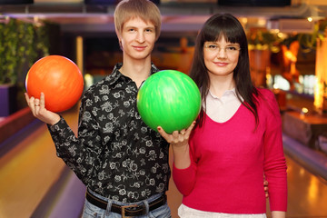happy wife and husband with balls stand in bowling club