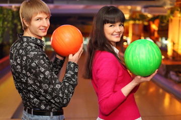 happy wife and husband with balls in bowling club stand sideways