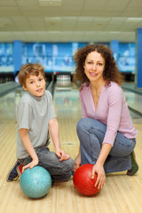 mother and son keep balls ant sit on floor in bowling club