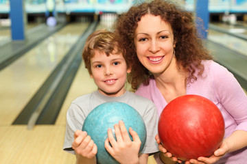 beautiful young mother and son keep balls in bowling club