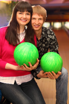 smiling young wife and husband with balls sit in bowling club
