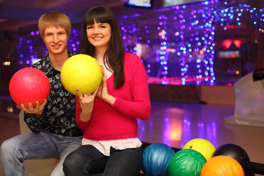 smiling young wife and husband with balls sit in bowling club