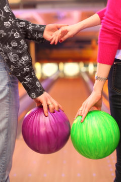 Female and male hands with balls in bowling club; man and woman
