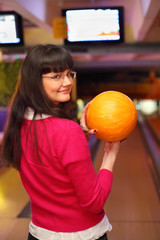 happy girl with ball stands back to camera in bowling club