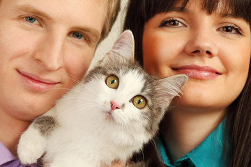 Smiling young husband and wife hold surprised cat; focus on cat