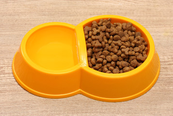 dry cat food and water in yellow bowl on wooden background