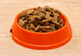 dry dog food in orange bowl on wooden background