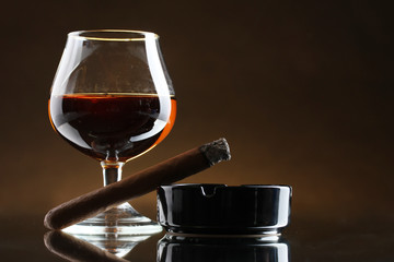 glass of brandy and cigar on brown background