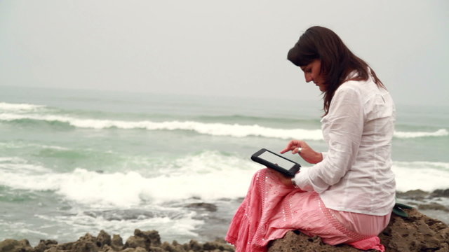 Attractive woman working on tablet computer on rocks at the sea