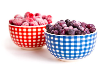 frozen raspberries and bilberries in the bowl, on a white backgr