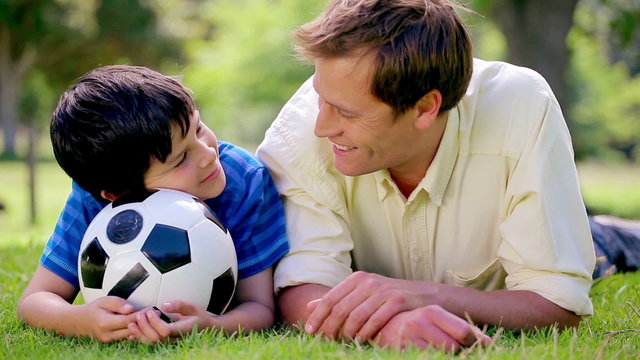 Happy father and son lying on the grass with a soccer ball