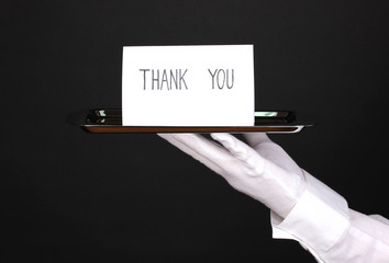 Hand in glove holding silver tray with card saying thank you