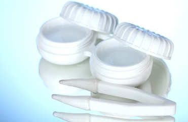 contact lenses in containers and tweezers on blue background