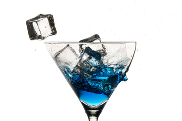 Ice cubes and broken martini glass with blue liqueur on white ba