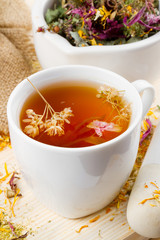 cup of healthy tea, mortar and pestle with healing herbs on wood