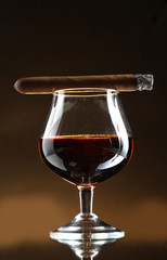 glass of brandy and cigar on brown background