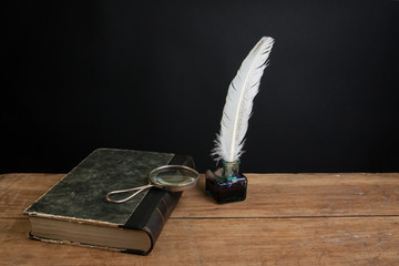 Quill and inkwell, old book and magnifying glass