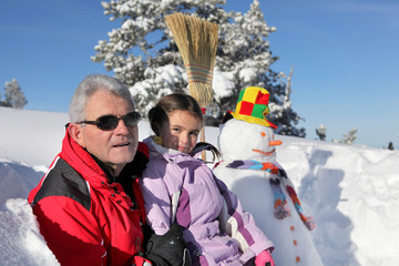 Father and daughter stood by snowman