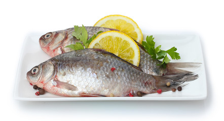 Fresh fishes with lemon and parsley on plate isolated on white