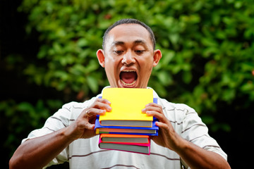 ethnic young man try to eat stack of books