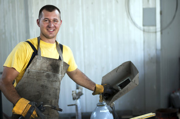 Smiling young happy satisfied welder at work - obrazy, fototapety, plakaty