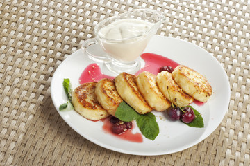 Sweet cheese pancakes on a plate   with sour cream and a cherry