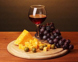 Wine in wineglass and cheese on wooden table on brown background