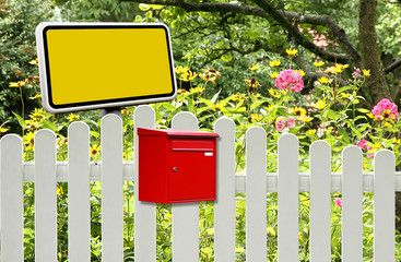 Roter Briefkasten und gelbes Schild am Gartenzaun
