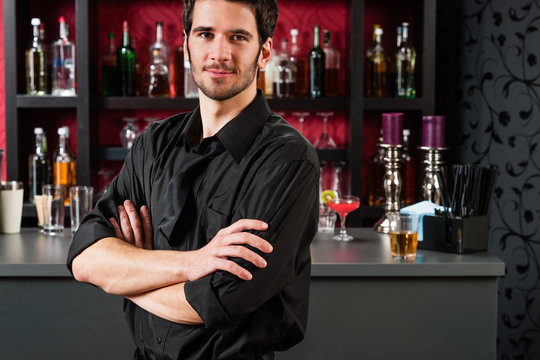 Barman in black standing at cocktail bar