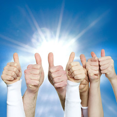 Close up of hands showing thumbs up in front of blue sky
