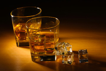 two glasses of scotch whiskey and ice on wooden table
