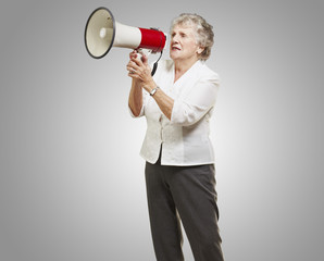 portrait of senior woman holding megaphone over grey background