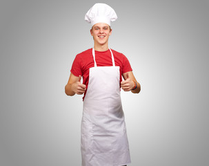 portrait of young cook man doing success symbol over grey backgr