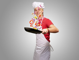 portrait of young cook man cooking vegetables on pan over grey b
