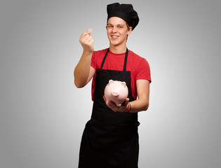portrait of young cook man holding euro coin and piggy bank over