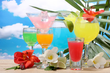 exotic cocktails and flowers on table on blue sky background