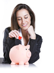 Close-up of young woman putting a red hearth  into a piggy bank,