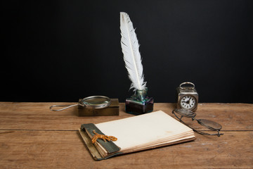 Notepad, quill, inkwell, magnifying glass, clock, specs on wood