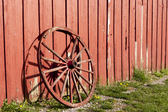 Old rustic wagon wheel beside a red barn.
