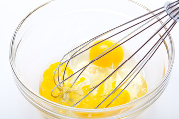 Wire whisk and brown eggs, isolated on white.