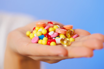 Pills, tablets and drugs heap in doctor's hand on blue backgroun